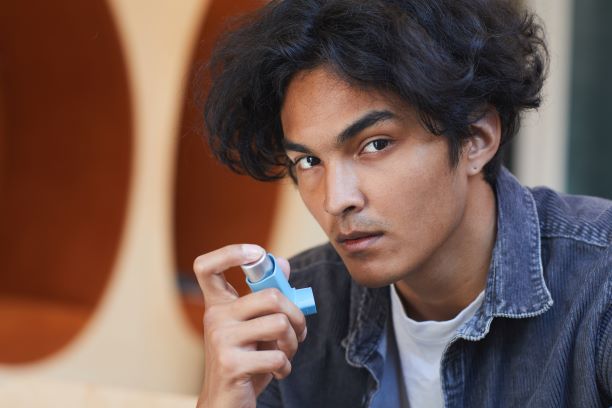 Young man having asthma, and using an asthma inhaler that turns asthma medicine into a spray, to help him breath better.