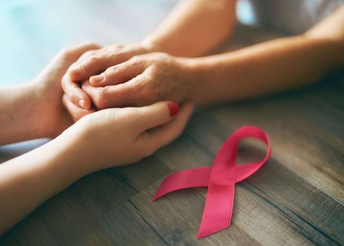 A person holding hands of a cancer patient to show solidarity and care. Cancer ribbon as a sign of support and awareness.