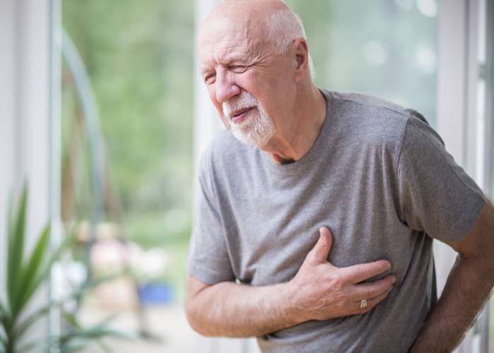 Man holding his heart with pain symptoms showing. He suffers from heart disease or having a heart attack or heart burn.