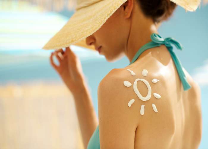 Woman wearing a hat to protect her face from the sun, and protecting her skin by putting sunscreen cream.