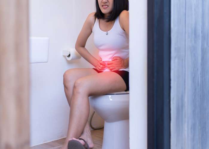 Woman suffering from constipation, sitting in pain on toilet seat and putting her hands on her stomach.