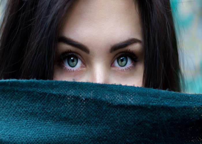 Eye disorder - eye health: woman hiding her face behind a piece of clothes and showing her beautiful blue eyes.
