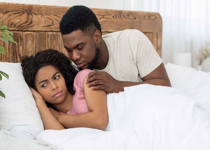 Man and woman sitting in bed. Man approaching the woman but she is showing no sexual desire. Low libido and sex drive.