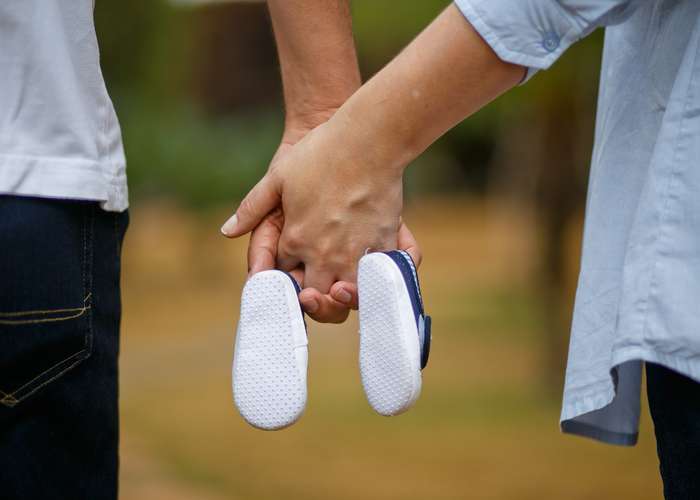 Couple walking holding hands, carrying new born baby shoes. Working to improve the man fertility to be able to have a baby.