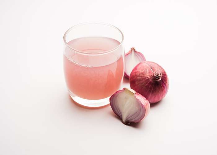 Onion benefits and side effects. Onion juice in a glass and onions next to it.