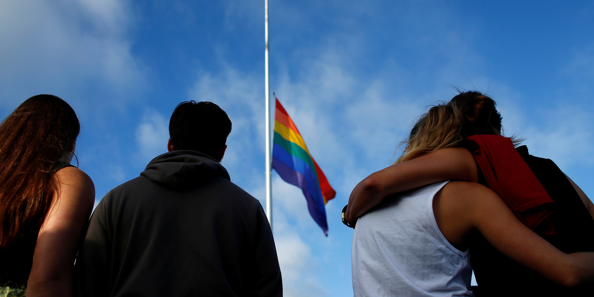 Mourners gather under a LGBT pride flag flying at half-mast for a candlelight vigil in remembrance for mass shooting victims in Orlando, from San Diego, California