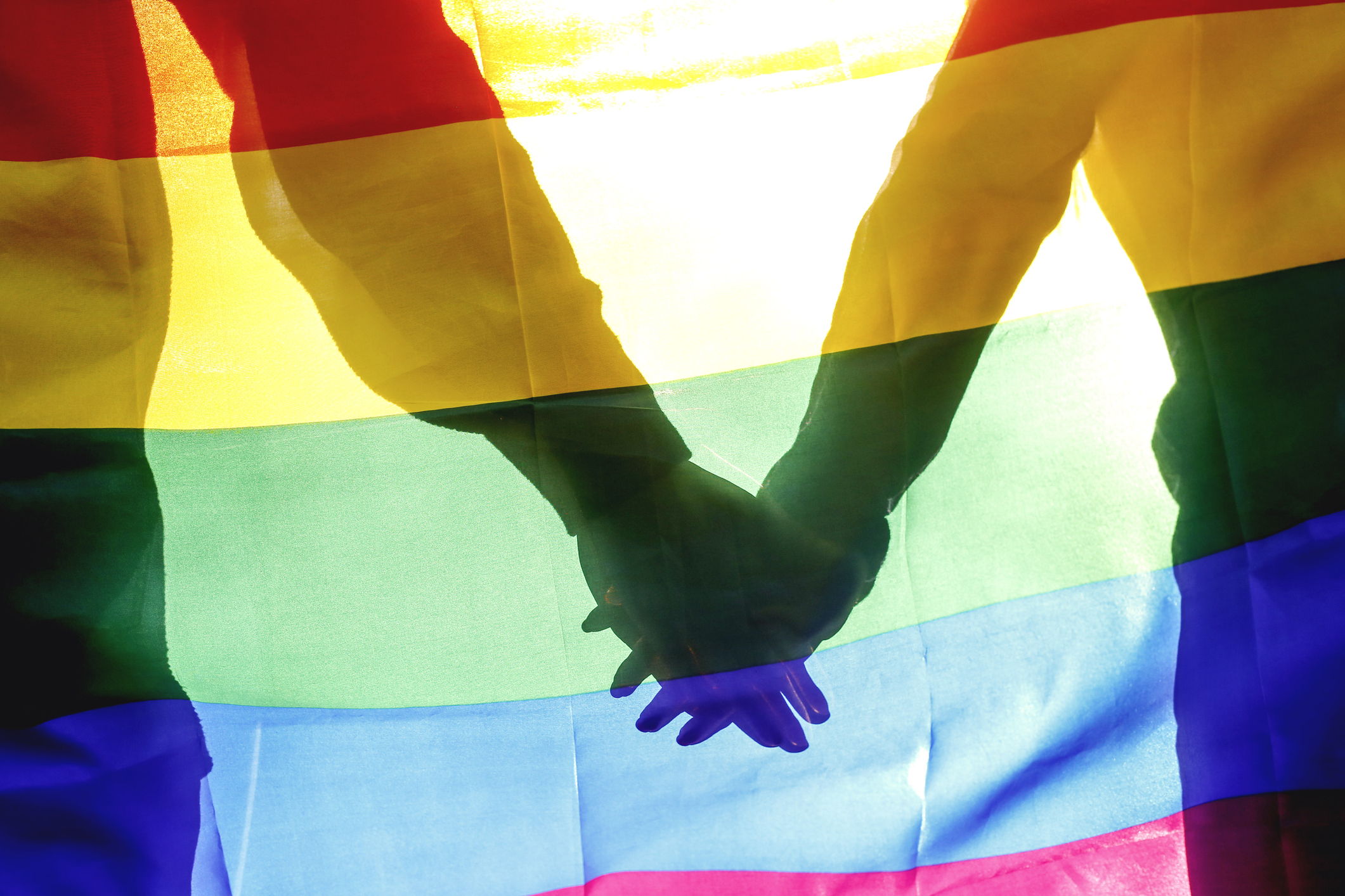 People, homosexuality, same-sex marriage, gay and love concept – close up of happy male gay couple hugging and holding rainbow flag