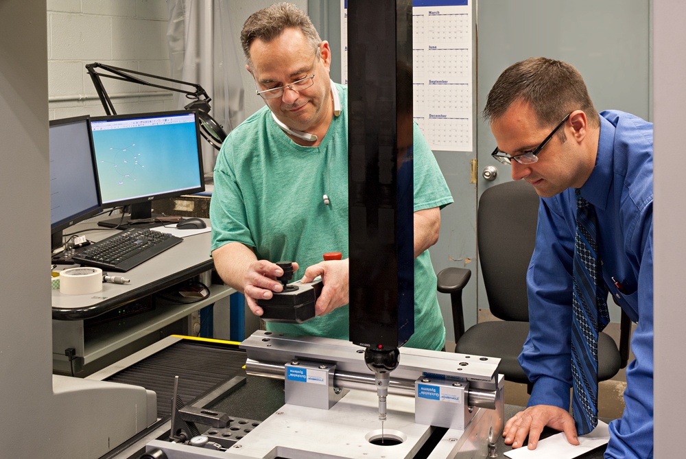 Quality and mechanical engineers inspecting a metal part on a CMM machine