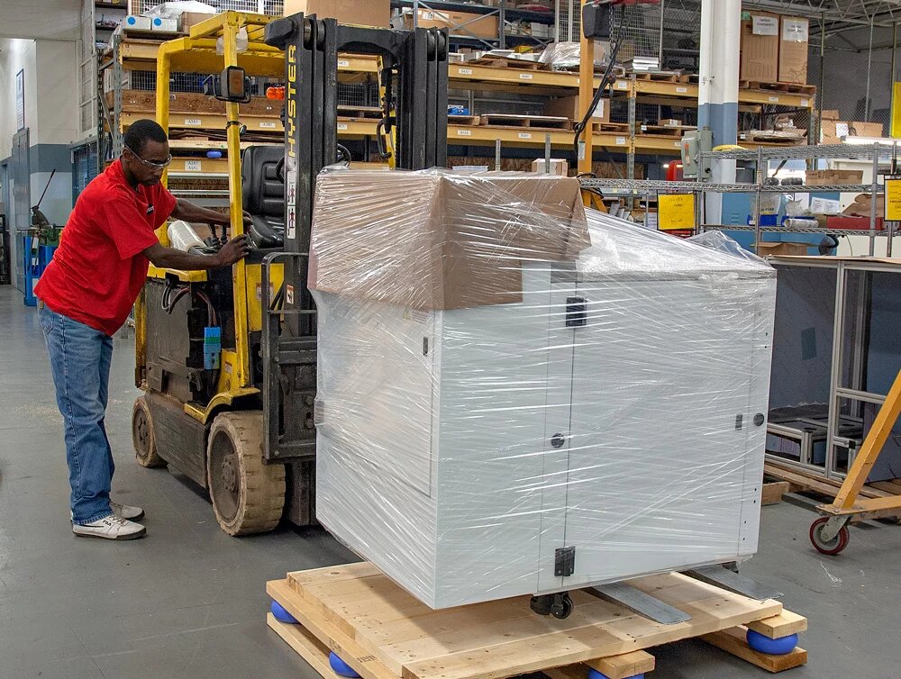 Worker packaging a white machine onto a forklift to ship to product's end user