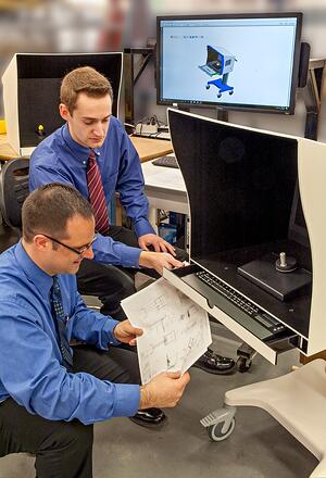 Two engineers reviewing a design's print with two machines