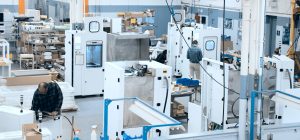 Four large white machine builds on the manufacturing floor with assemblers