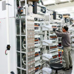 Technicians assembling and integrating a row of complex electromechanical prototype machine builds with integrated wiring and control hardware.