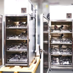 Interior view of two open battery test chambers showing organized fixture trays, wiring, and port access for module testing.