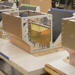 Row of aluminum sheet metal chassis with rivets and fasteners on an assembly table—an example of precision custom fabrication.