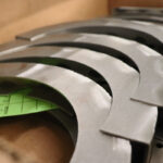 Stacked curved steel ring segments with pilot holes and deburred edges in a box, ready for assembly—custom sheet metal fabrication.