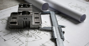 Machined metal component on engineering drawings with calipers, showing the reverse engineering process for mechanical parts and CAD documentation.