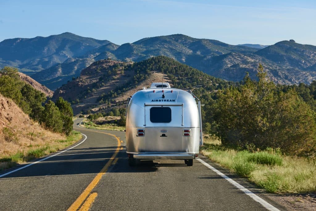 A towable Airstream RV winds through the mountains.