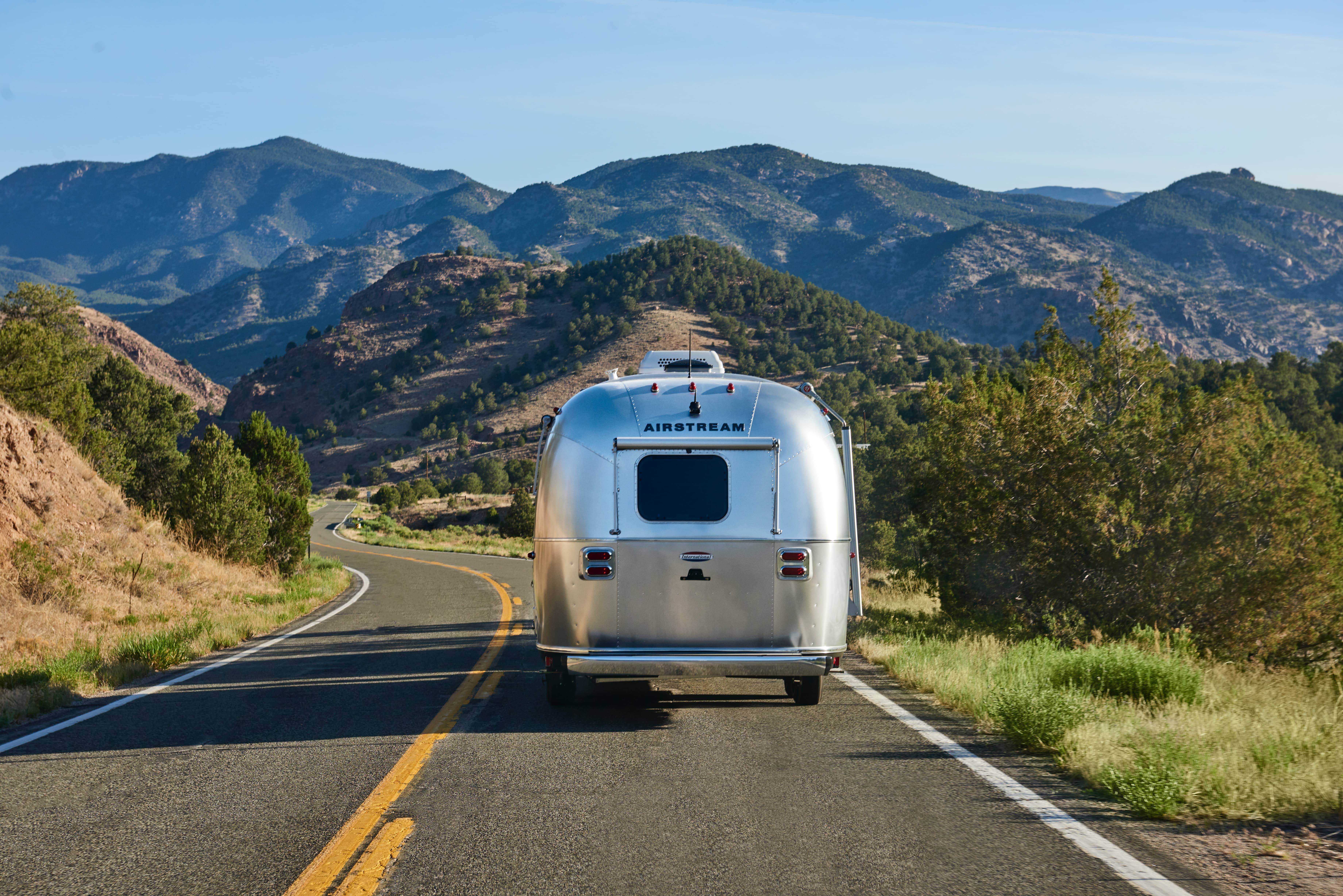 A towable Airstream RV winds through the mountains. 