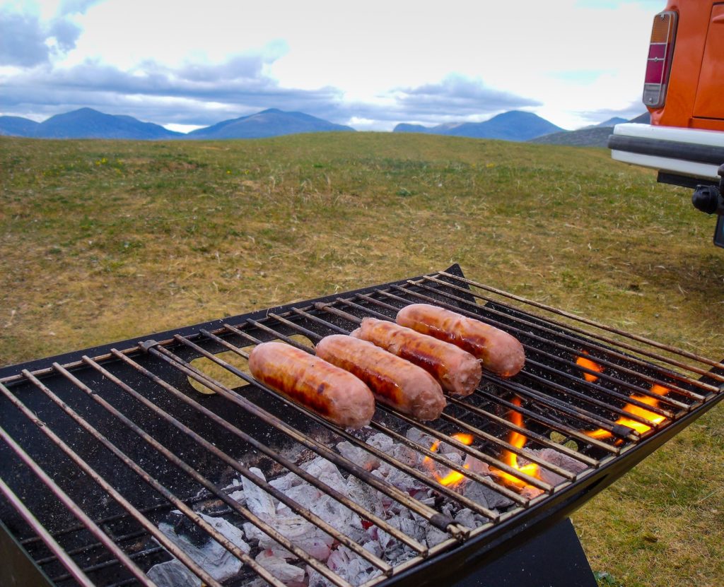 Four delicious sausages cooked to perfection on the traditional charcoal barbecue fiery grill.  This scene on a camping road trip to the mountains. A typical Summer image when camping, travelling or having parties with family and friends.