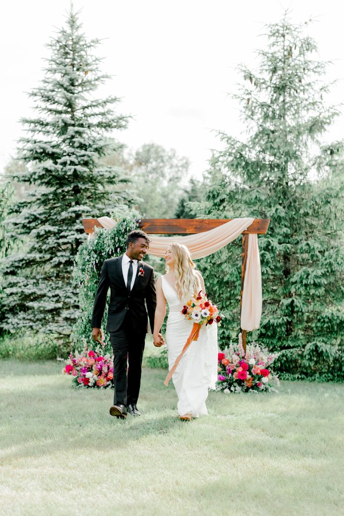 Bride and Groom Walking Under Wooden Wedding Arch While Bride Wearing Boho Lace Wedding Dress Burke by Maggie Sottero