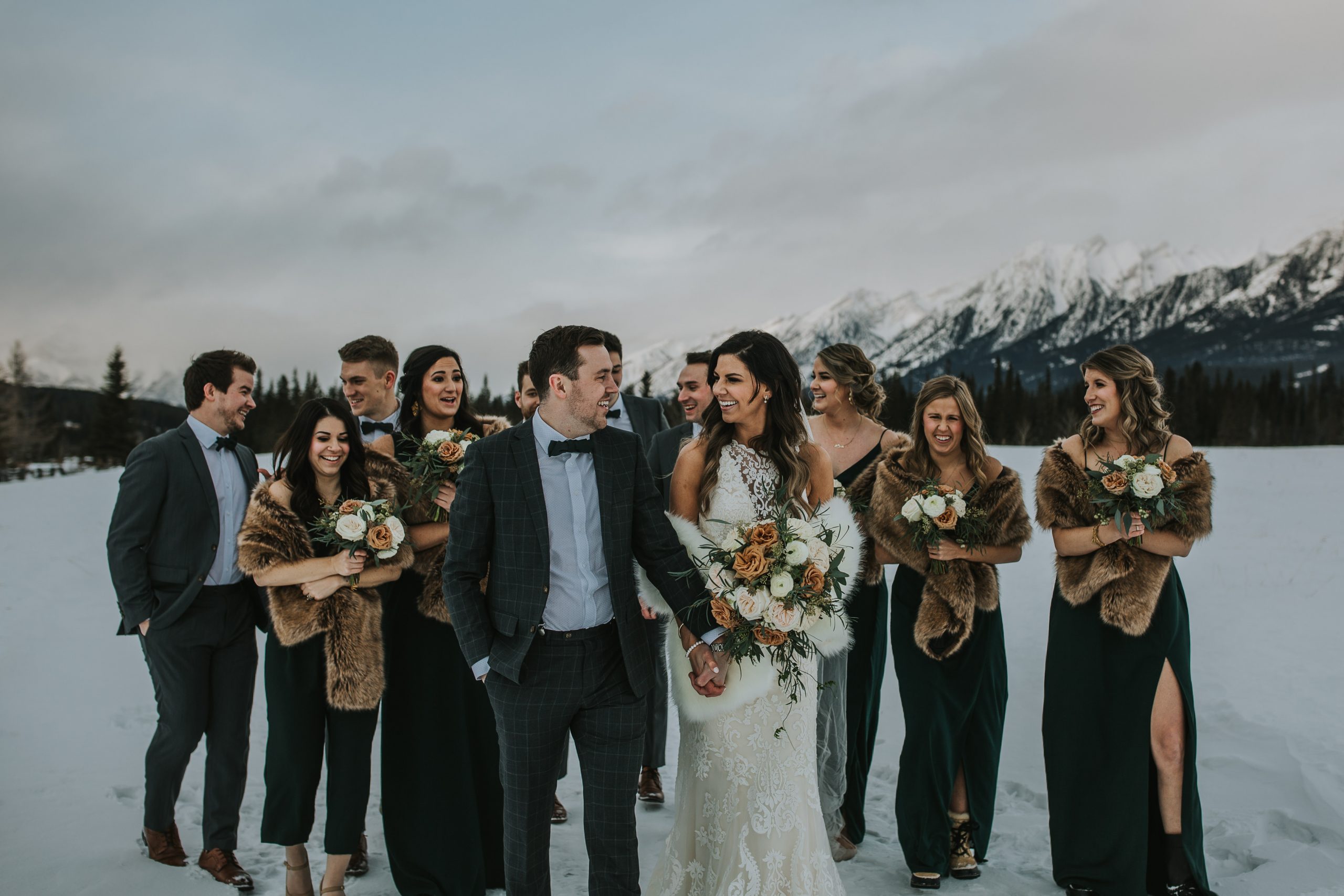 Bride Wearing Halter Neck Wedding Dress by Sottero and Midgley Walking with Groom in the Snowy Mountains Walking Through Arch Made by Wedding Party