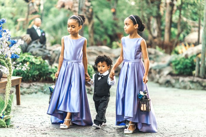Flower Girls Wearing Purple Dresses Walking with Little Ring Bearer at Fairytale Wedding