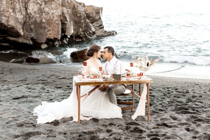 Bride and Groom on Black Sand Beach Looking at Each Other and Sitting at a Reception Table