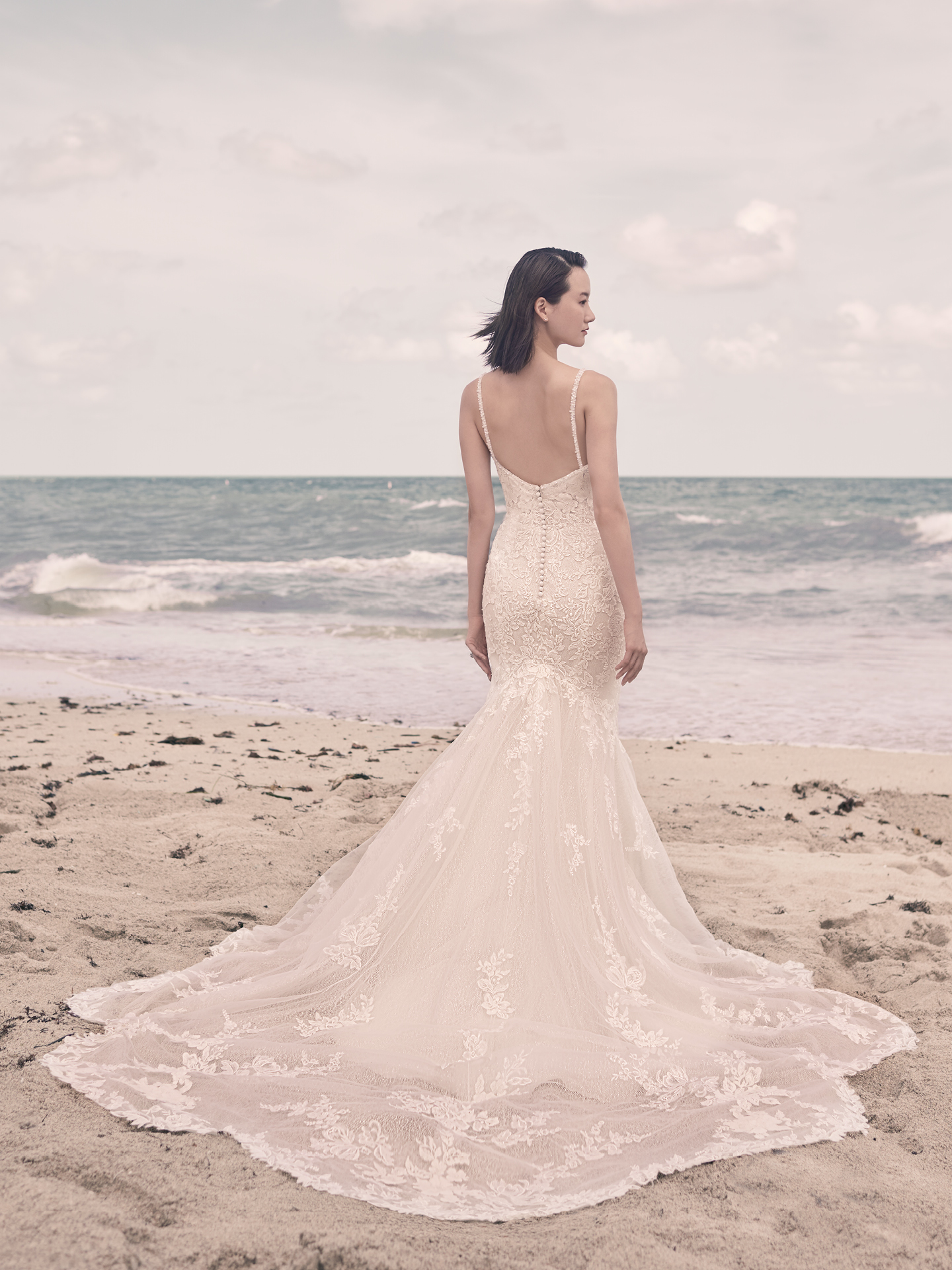 Model on Beach Wearing Lace Mermaid Wedding Dress with Long Train Called Bryan by Sottero and Midgley