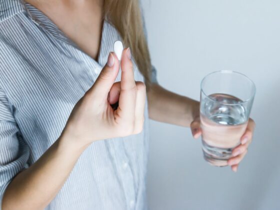 woman holding half full glass and white medicine pill