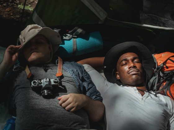 multiethnic male backpackers napping on rucksacks in soft sunlight