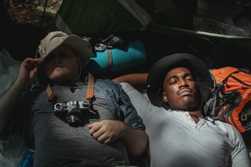 multiethnic male backpackers napping on rucksacks in soft sunlight