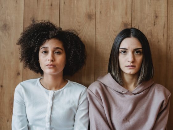 multiethnic thoughtful ladies sitting near wooden wall