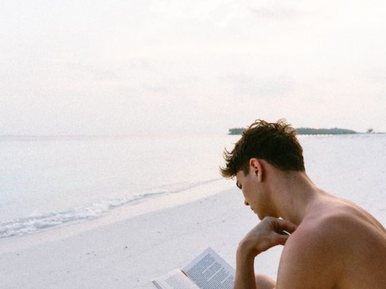 topless man reading book while seating at beach