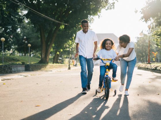 man standing beside his wife teaching their child how to ride bicycle