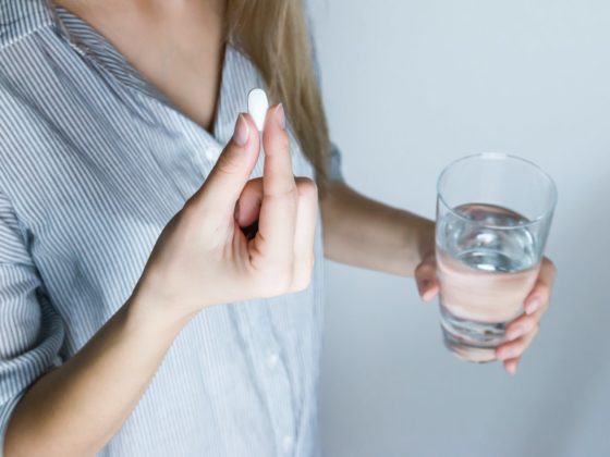 woman holding half full glass and white medicine pill