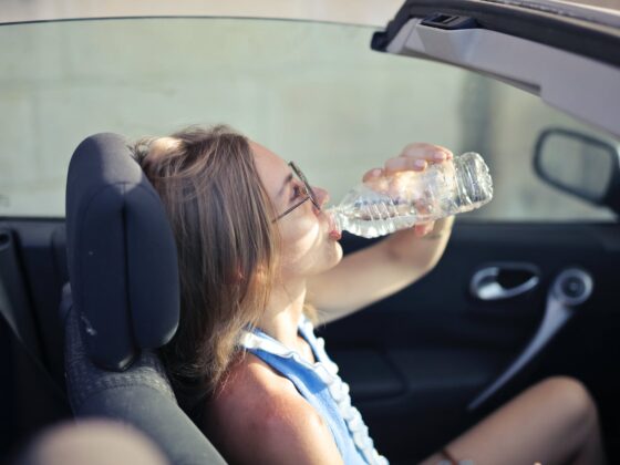 adult female drinking water in convertible car in city