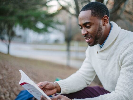 selective focos photography of man in white sweater reading book
