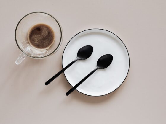 cup of coffee and plate with spoons on beige background