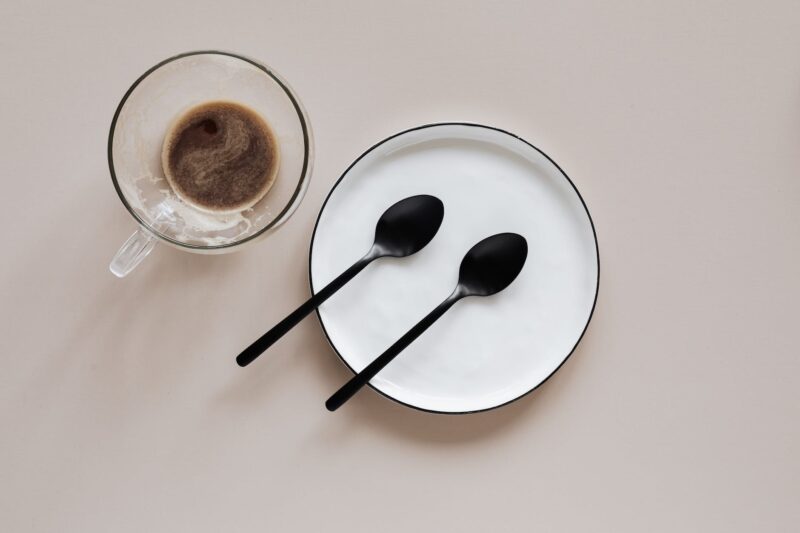 cup of coffee and plate with spoons on beige background