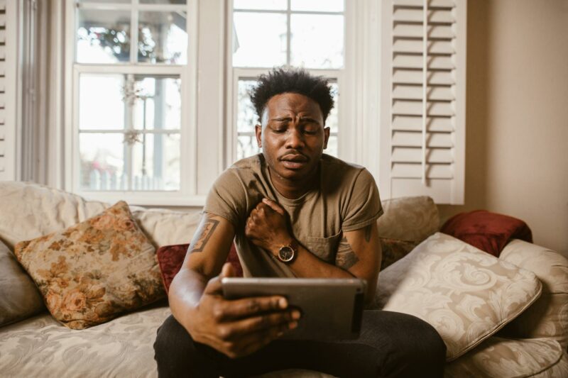emotional man sitting on couch watching a video on tablet