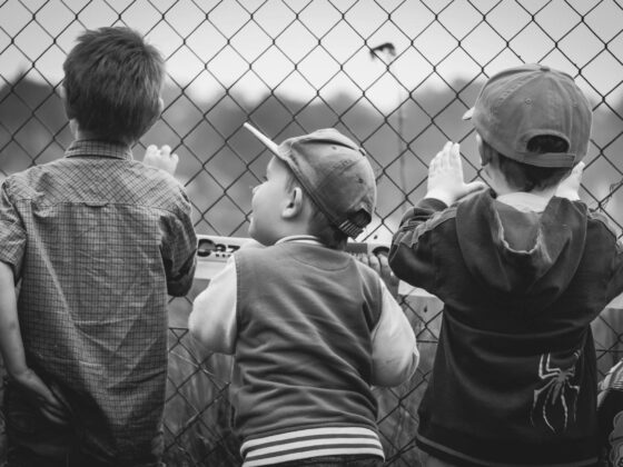 grayscale photography of three boys facing towards fence